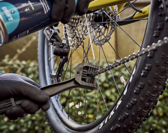 Fietsketting van een mountainbike die wordt schoongemaakt met een fietskettingborstel.